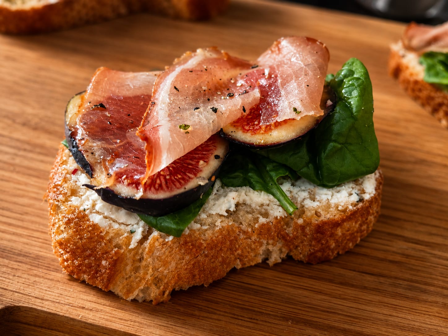 Tapa de pan con queso, higo, hojas verdes y jamón para acompañar una tabla